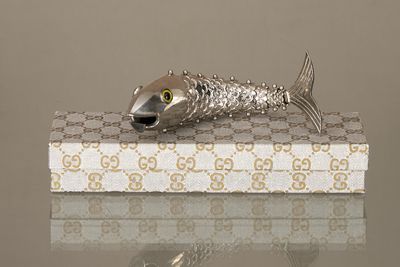 une figurine en argent représentant un poisson, posée sur une boîte