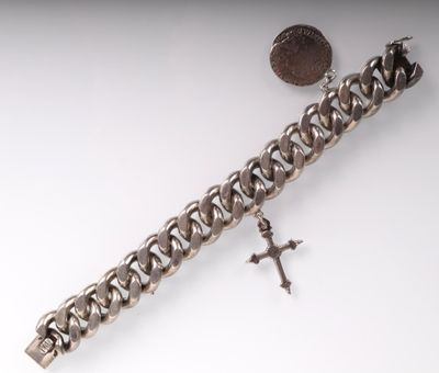 bracelet à chaîne en argent orné d'une croix et d'une pièce sur un fond blanc