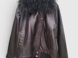 une veste en cuir marron avec un col en fourrure noire, suspendue à un cintre devant un mur blanc