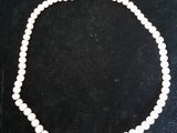 un collier de perles blanches avec un fermoir en or sur fond noir