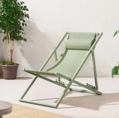 une chaise de jardin verte posée sur un tapis, à côté d'une plante en pot