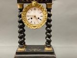 a black and gold clock on a stand with a pair of scissors next to it
