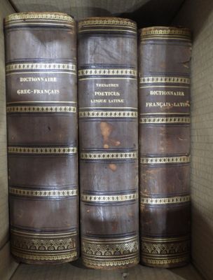 Plusieurs vieux livres sont empilés dans une boîte en carton posée sur une étagère