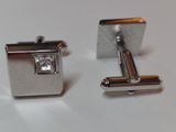 pair of silver cufflinks with a diamond on each of them