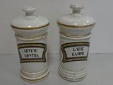 pair of white and gold ceramic jars with labels on them