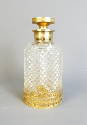 une bouteille en verre à l'ancienne avec un bouchon doré, posée sur une surface blanche
