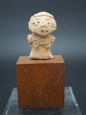 une petite statue en pierre représentant un homme coiffé d'un chapeau, posée sur un bloc de bois
