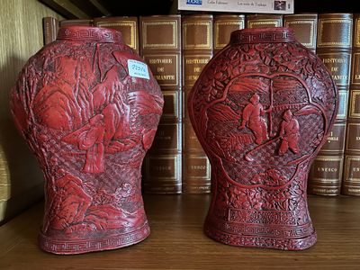 deux vases rouges posés sur une étagère devant des livres