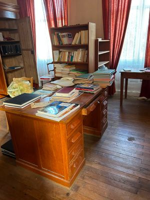 un bureau sur lequel sont posés de nombreux livres, dans une pièce