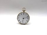 une petite montre de poche en or posée sur une surface blanche