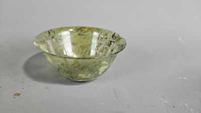 green glass bowl sitting on top of a table next to a white wall