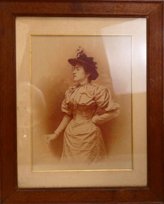 une vieille photo représentant une femme en robe et chapeau, dans un cadre en bois