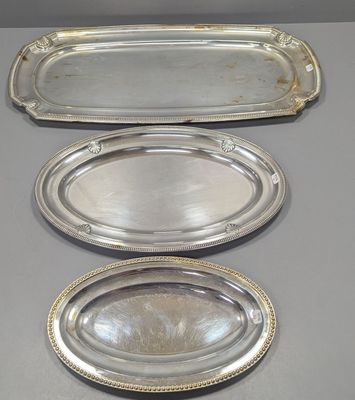 trois plateaux en argent munis d'anses, posés sur une table
