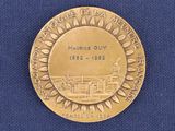gold medal with a picture of a town on it on a blue cloth