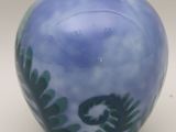 a blue vase with green leaves on it sitting on a table