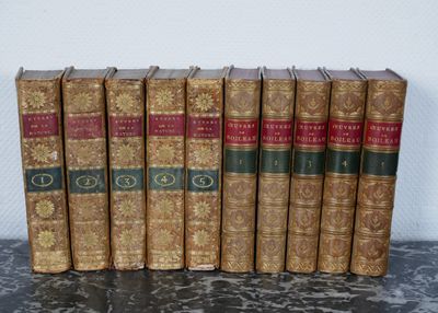 Plusieurs vieux livres sont alignés sur une table devant un mur blanc.