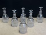 six carafes en verre transparent posées sur une table avec un fond noir