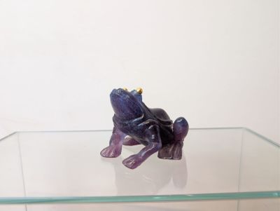 figurine de grenouille violette posée sur une étagère en verre dans une pièce blanche