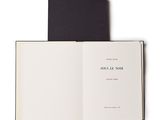 un livre ouvert posé sur une table blanche, à côté d'un livre noir