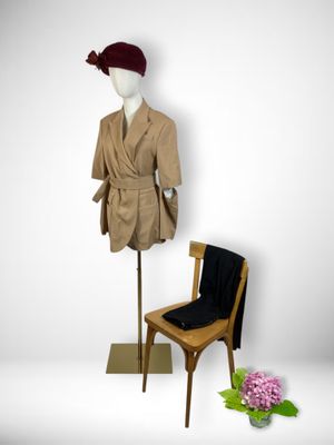 a mannequin sitting next to a chair and a coat on a stand