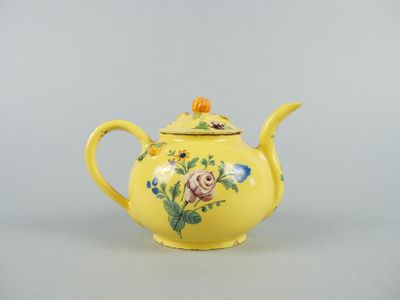 an old yellow teapot with flowers and leaves painted on it