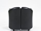 pair of black leather lounge chairs on casteors against a white background