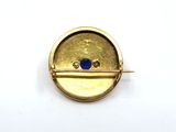 a close up of a gold plated brooch with a blue stone