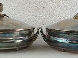 two silver dishes on a table with a white wall in the background
