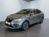 La voiture grise est garée dans le showroom, devant un mur blanc.