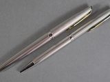 two silver pens sitting next to each other on top of a table