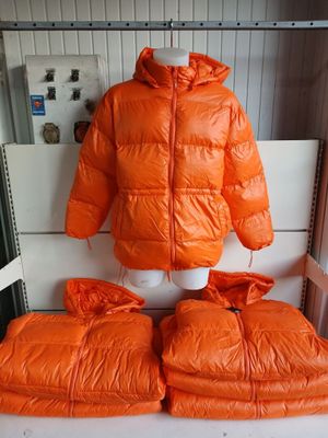 une veste orange posée sur un présentoir à mannequin, à côté d'une paire de coussins