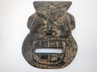 un masque en métal accroché à un mur sur fond blanc