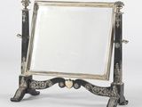 un miroir ancien argenté et noir posé sur un pied orné d'un cœur