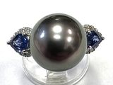une image d'une bague ornée d'une perle noire et d'un saphir, posée sur un socle transparent