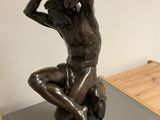 bronze statue of a woman sitting on a rock with her hands on her head