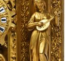 a gold clock with a woman playing a musical instrument