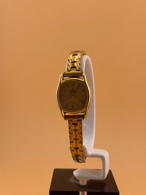 une image représentant une montre en or posée sur un socle blanc, sur un fond marron