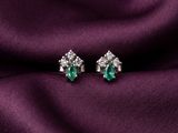 a pair of emerald and diamond earrings on a purple silk