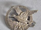 une image représentant une broche en argent sur laquelle figurent un oiseau et un autre oiseau perché sur une branche