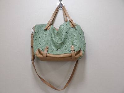green leather handbag hanging on a wall with a wooden handle