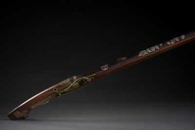 un fusil avec un canon en bois et des garnitures en laiton sur fond noir