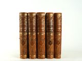 four old books are lined up in a row on a white surface