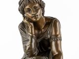 a bronze statue of a woman sitting on a rock with her hand on her chin