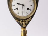 une horloge dorée et noire posée sur un socle, avec une paire de ciseaux