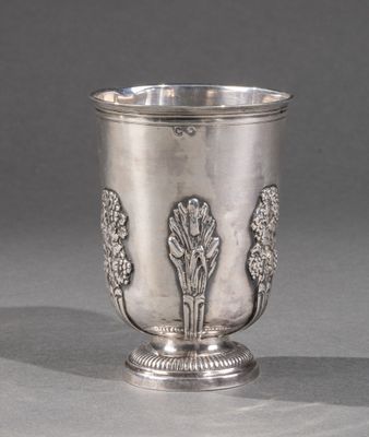 une coupe en argent ancienne posée sur une table, devant un fond gris