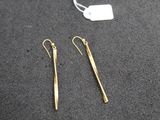 une paire de boucles d'oreilles en or posée sur une table, à côté d'une étiquette