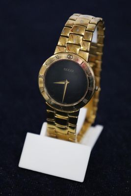 an image of a close up of a gold wrist watch on a stand