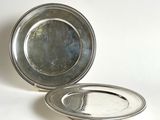 two silver plates sitting on a white surface