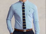 un homme en chemise bleue et cravate, debout, les mains dans les poches