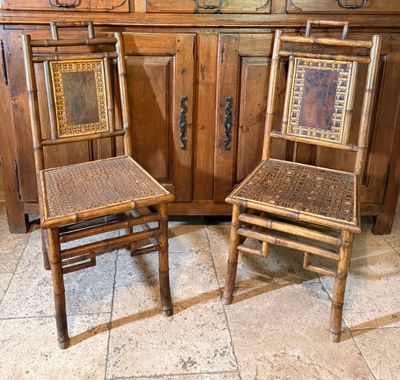 une paire de chaises anciennes en bambou avec des assises tressées, placées devant un meuble